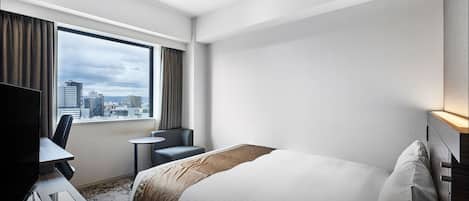 A hotel room with a bed, a desk with a chair, a TV, and a window with curtains.