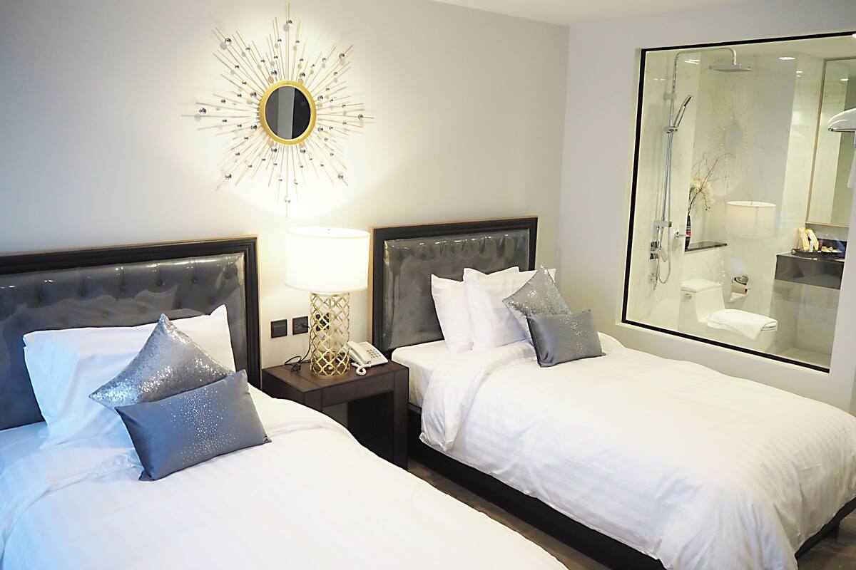 A hotel room with two beds, a large mirror, and a view of the bathroom.