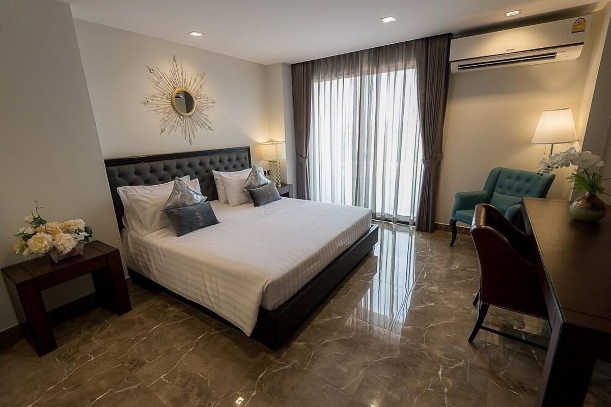 A hotel room with a large bed, a desk, a chair, a mirror, and a window with curtains.