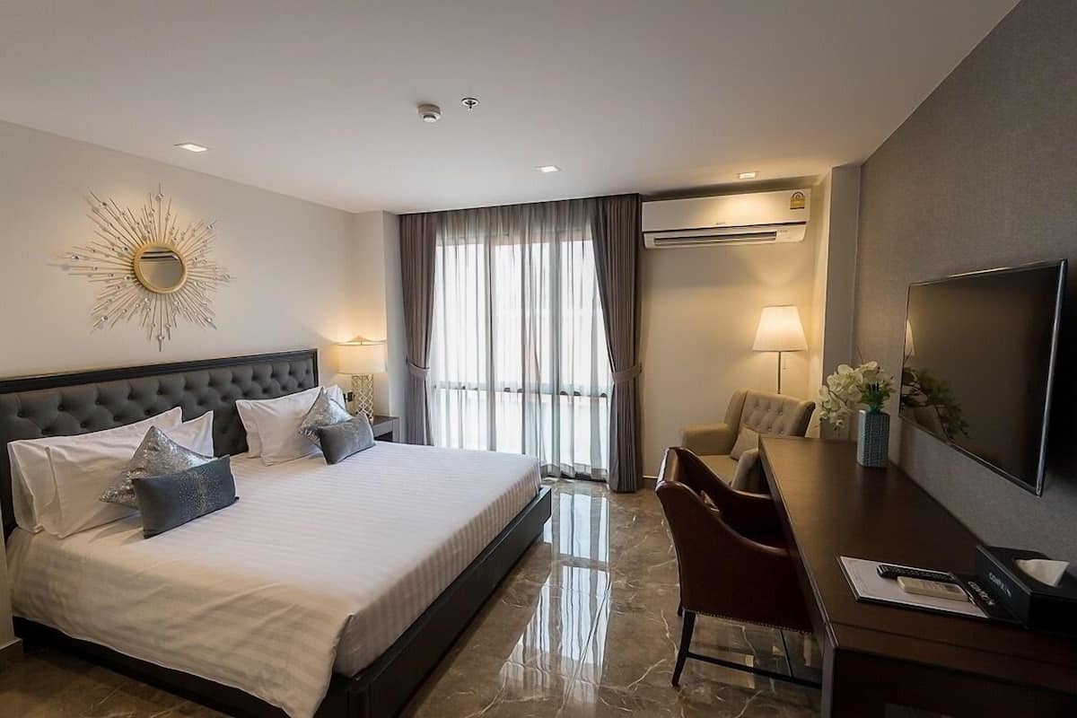 A hotel room with a large bed, a desk with a TV, a chair, and a sunburst wall decoration.