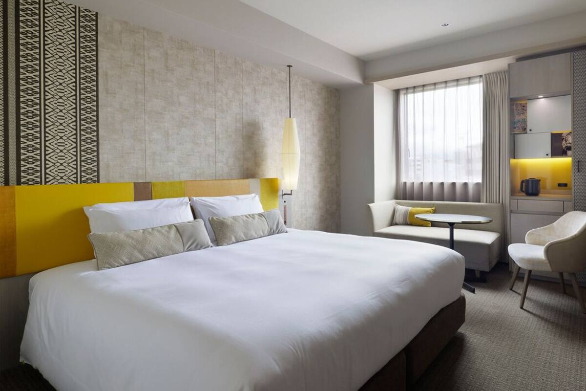 A hotel room with a large bed, a small table, a chair, a desk, and a window with curtains.