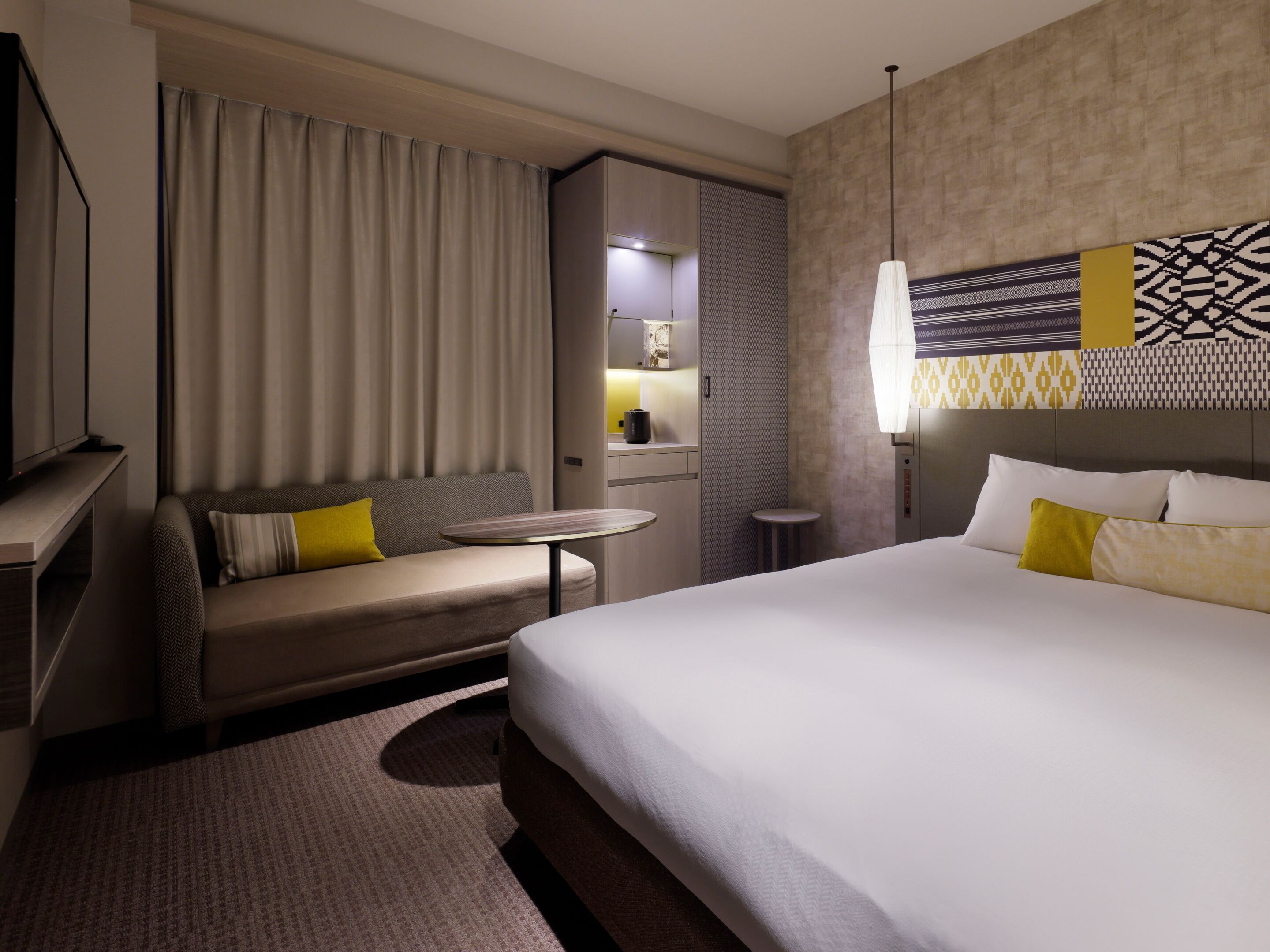A hotel room with a bed, a sofa, a small table, a TV, and a bathroom area.