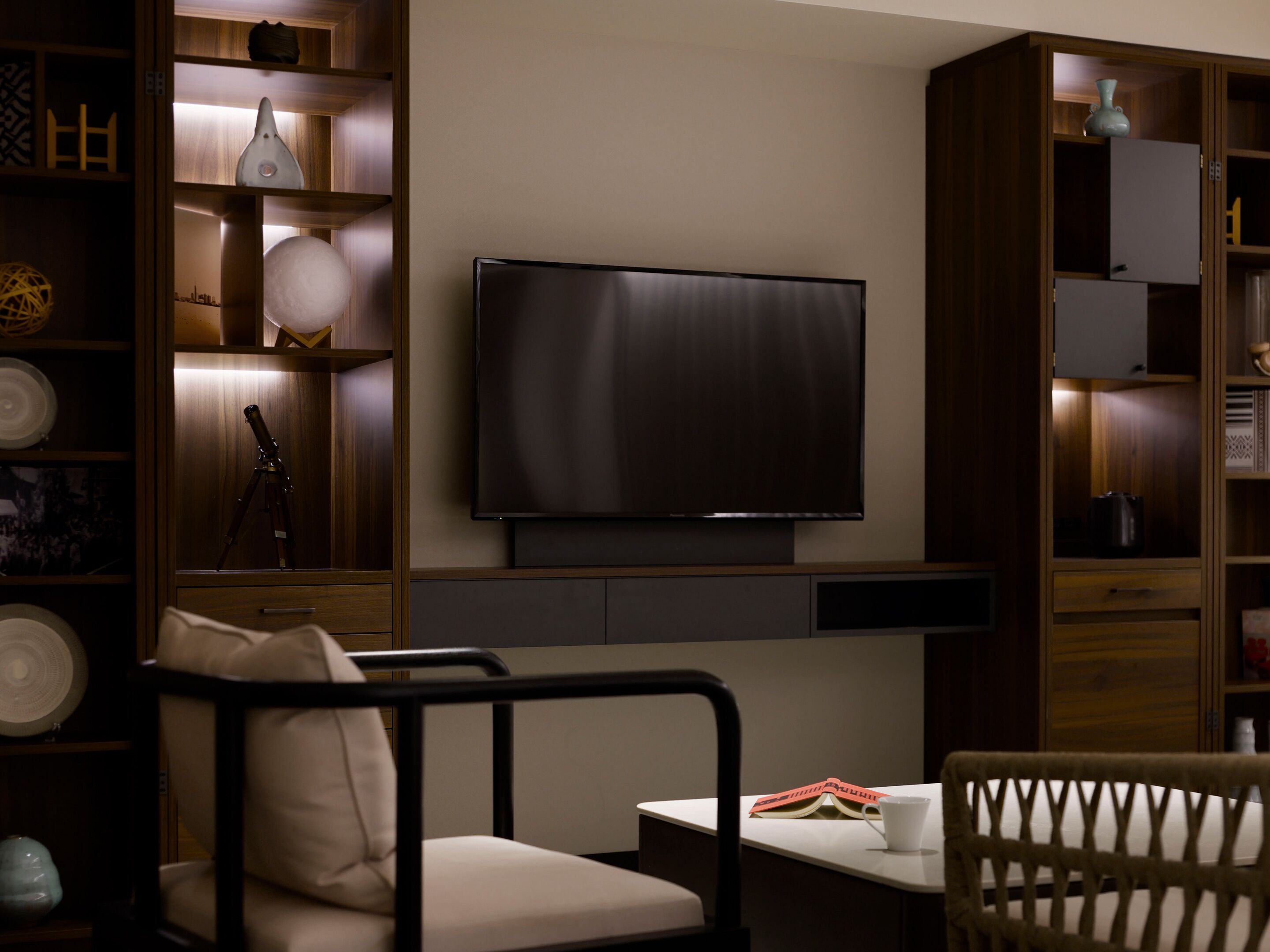 A modern living room with a flat-screen TV mounted on the wall, a sofa, a coffee table, and built-in wooden shelving with decorative items.