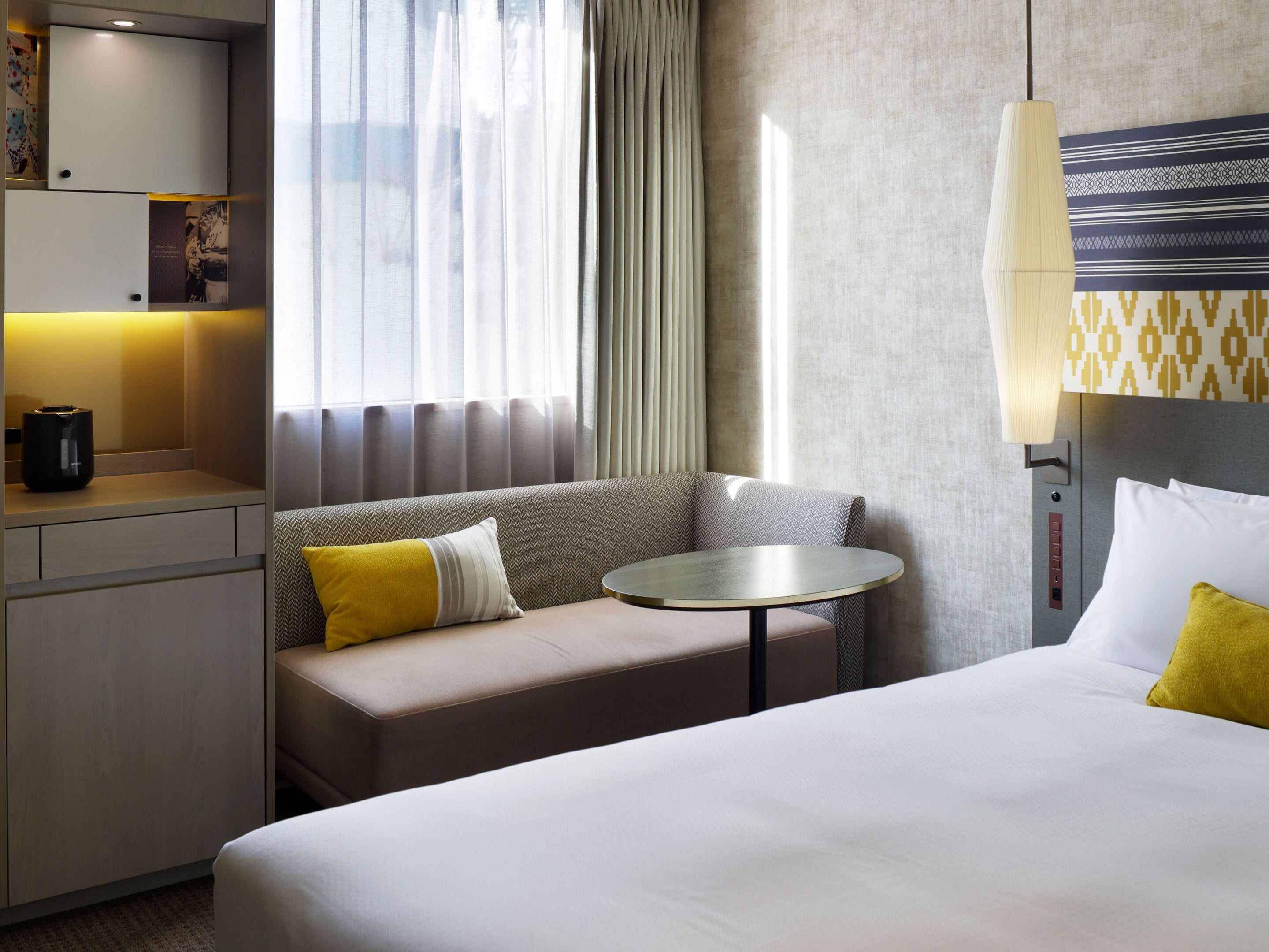 Ein Hotelzimmer mit Bett, einer Couch, einem kleinen runden Tisch, einer Lampe und einem Fenster mit Vorhängen.
