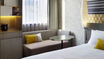 Ein Hotelzimmer mit Bett, einer Couch, einem kleinen runden Tisch, einer Lampe und einem Fenster mit Vorhängen.