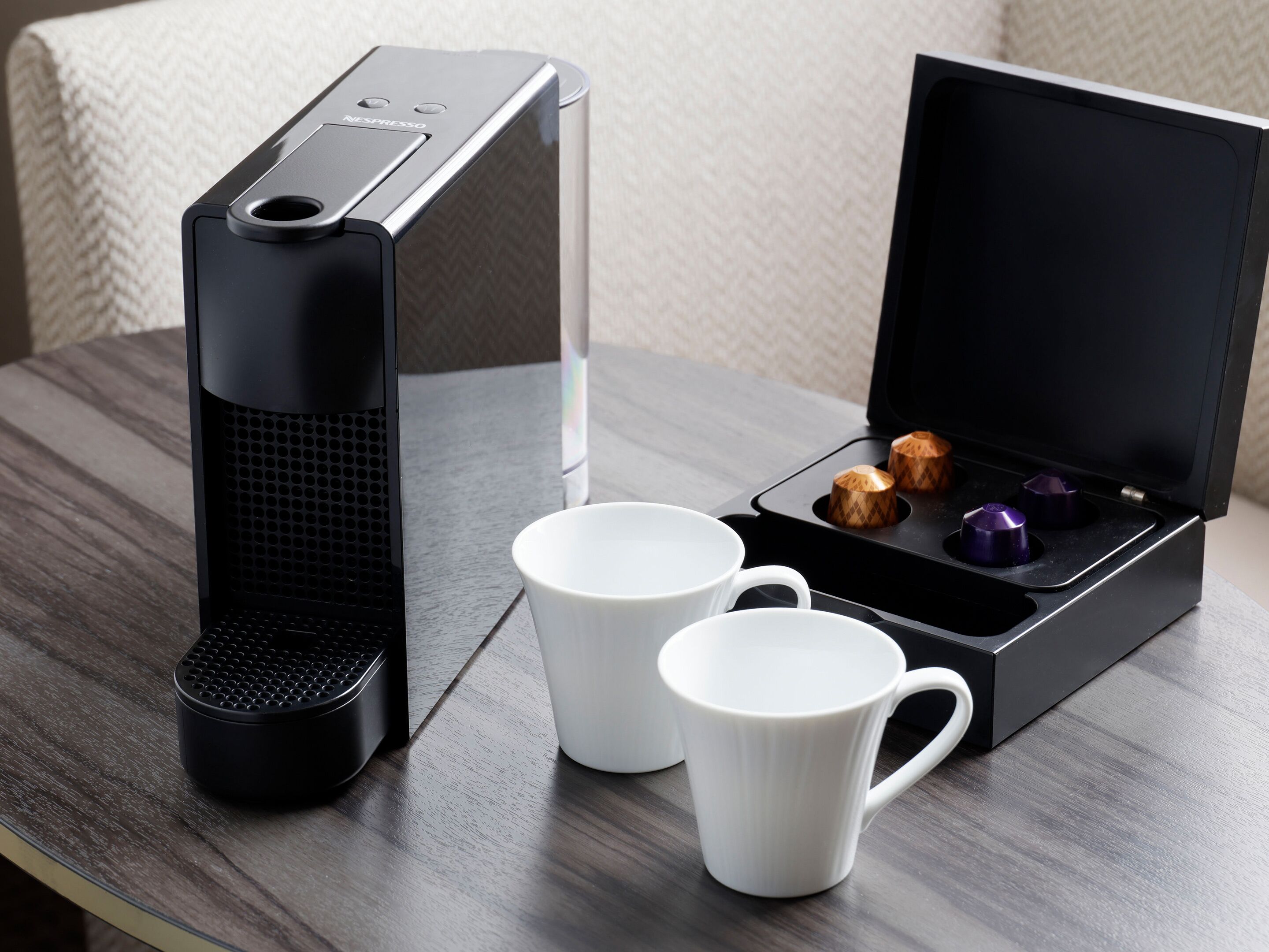 A Nespresso coffee maker with two white mugs and a box containing two capsules.