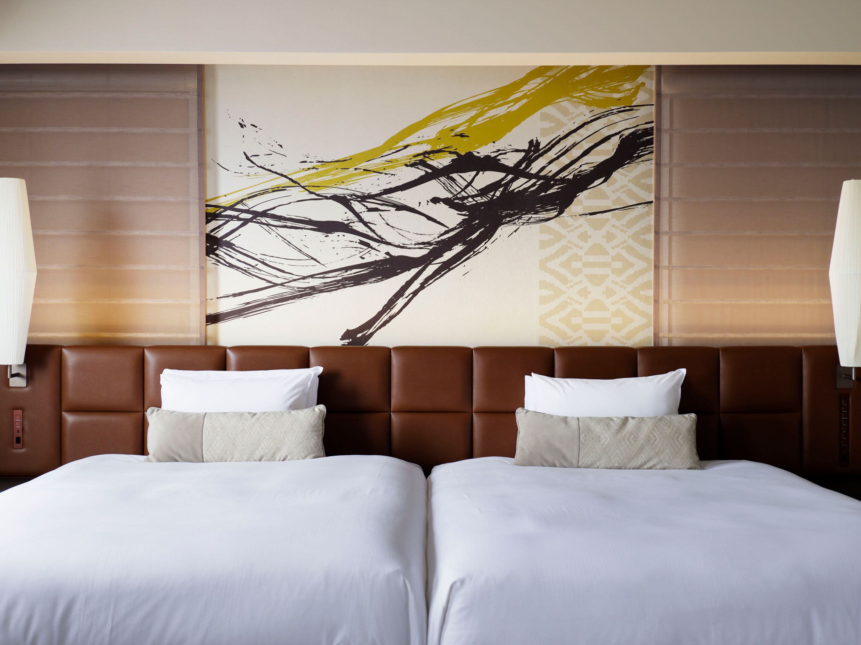 Habitación de hotel con un cuadro abstracto grande en la pared, dos camas con ropa blanca y un cabecero marrón.