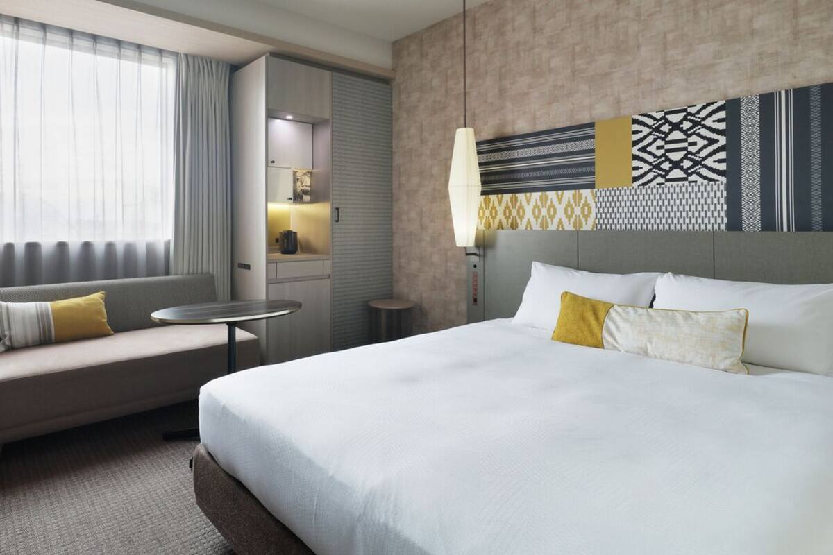 A hotel room with a bed, a sofa, a small table, a TV, and a window with curtains.