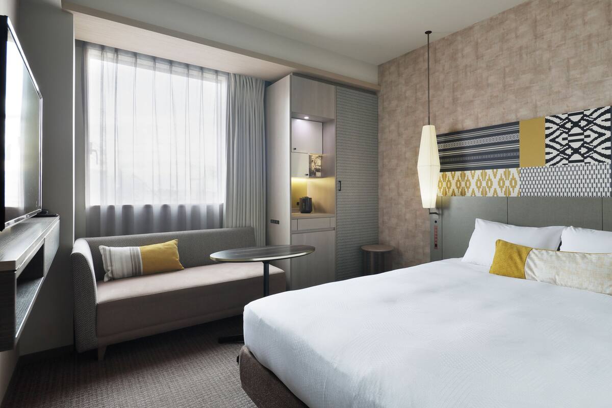 Ein Hotelzimmer mit Bett, Sofa, kleinem Tisch, Fernseher und einem Fenster mit Vorhängen.