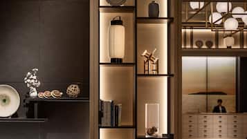A modern interior with a dark wall, a wooden bookshelf with decorative items, and a reception area with a person in the background.