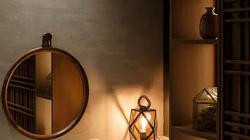 A round mirror, a wall-mounted light fixture, and a shelf with a vase and a glass container.