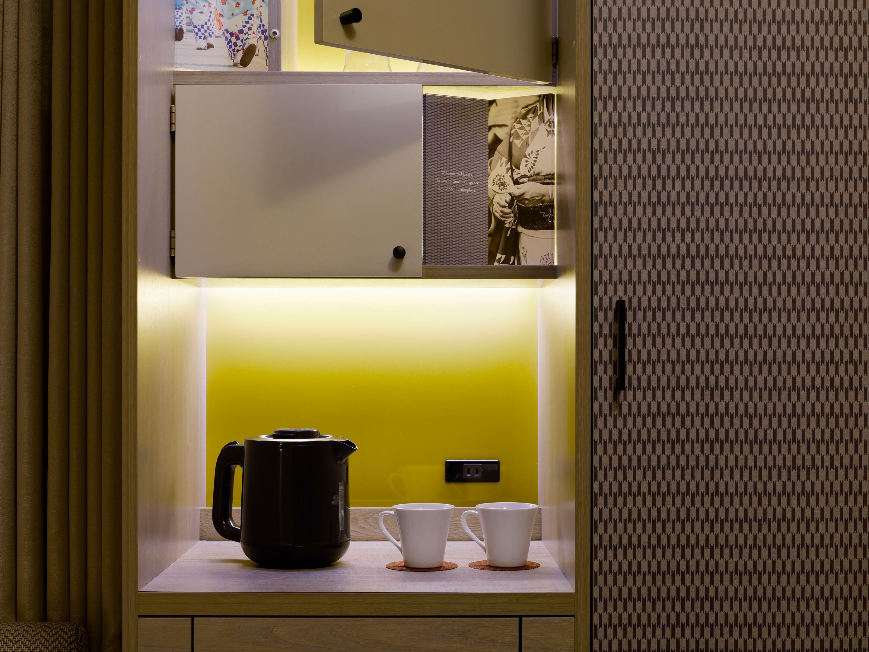 A kitchenette with a coffee maker, two cups, and a power outlet.