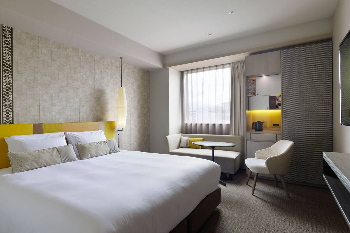 Ein Hotelzimmer mit einem großen Bett, einem kleinen Tisch, einer Couch, einem Sessel und einem Schreibtisch mit einer Lampe.