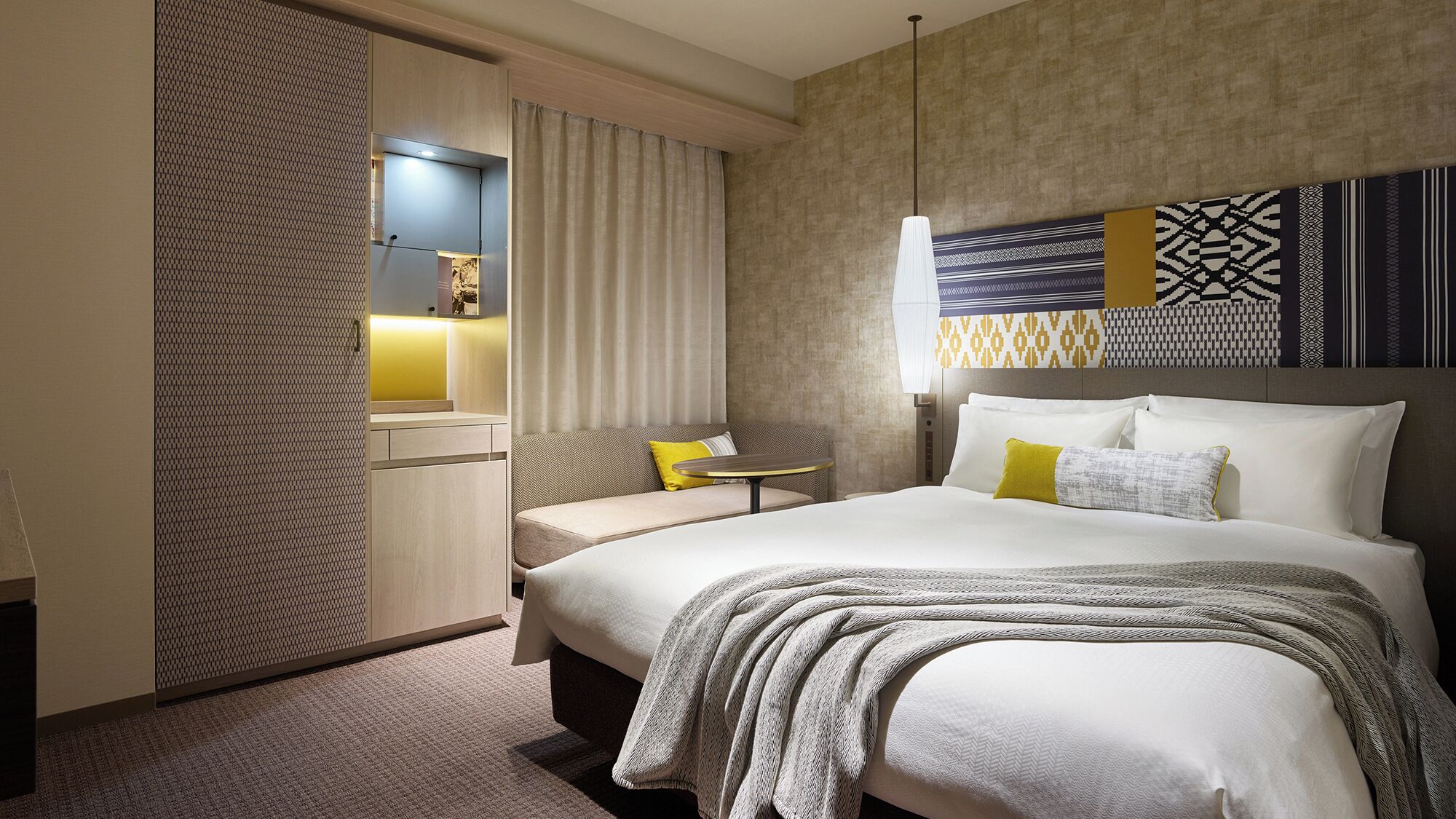 A hotel room with a bed, a sofa, a small table, and a wall-mounted TV.