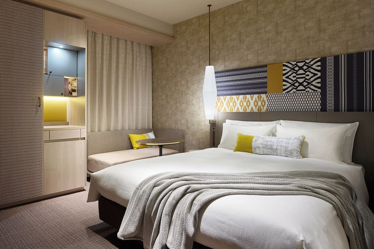 Habitación de hotel con cama, sofá, una mesita y televisor montado en la pared.