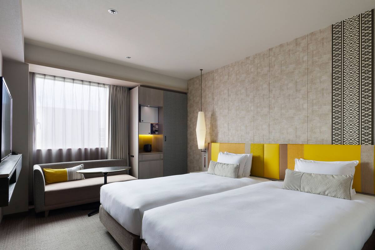 Ein Hotelzimmer mit zwei Betten, einem Sofa, einem Schreibtisch und einem Fernseher.