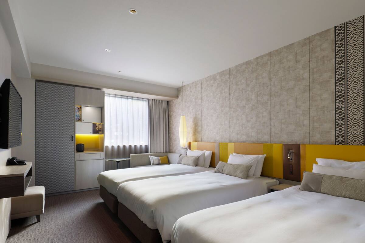 Ein Hotelzimmer mit zwei Betten, einem Schreibtisch, einem Sessel, einem Fernseher und einem Fenster mit Vorhängen.