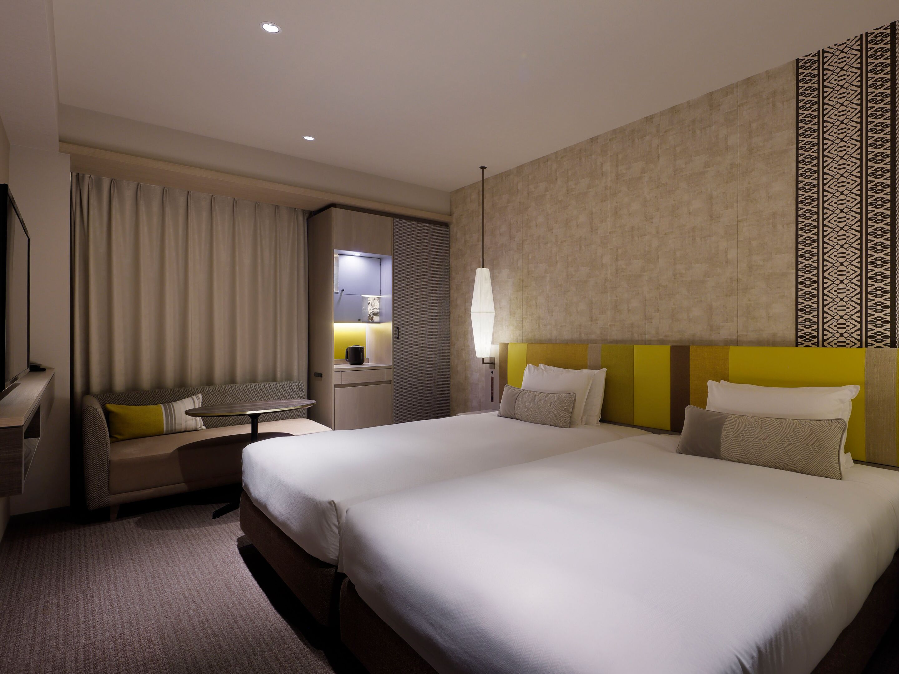 A hotel room with a large bed, a desk, a chair, a small table, and a mirror.