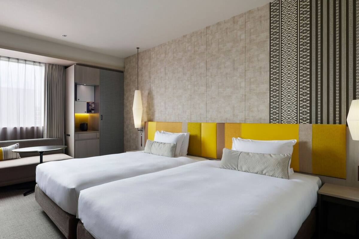 A hotel room with two beds, a desk, a sofa, and a TV.