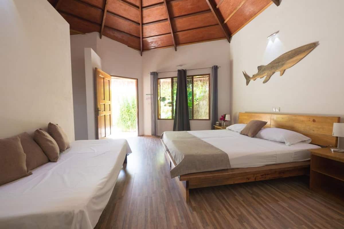 Quarto com duas camas, piso de madeira, teto de madeira, janela com cortinas e um peixe decorativo na parede.