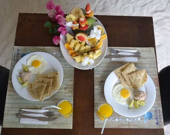 A breakfast setting with plates of eggs, toast, and fruit, along with a decorative flower arrangement. - Blue World Dharavandhoo (Dharavandhoo)