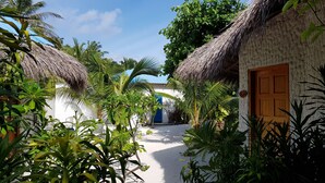 A tropical garden with thatched-roof huts, a white building with a blue door, and lush greenery.