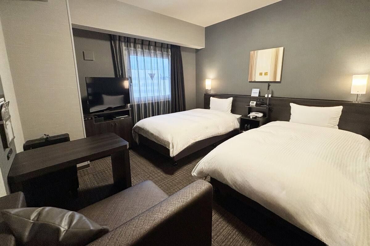 A hotel room with two beds, a TV, a desk, and a chair.
