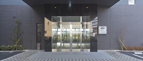 A modern building entrance with a glass door, a tiled floor, and a signboard.