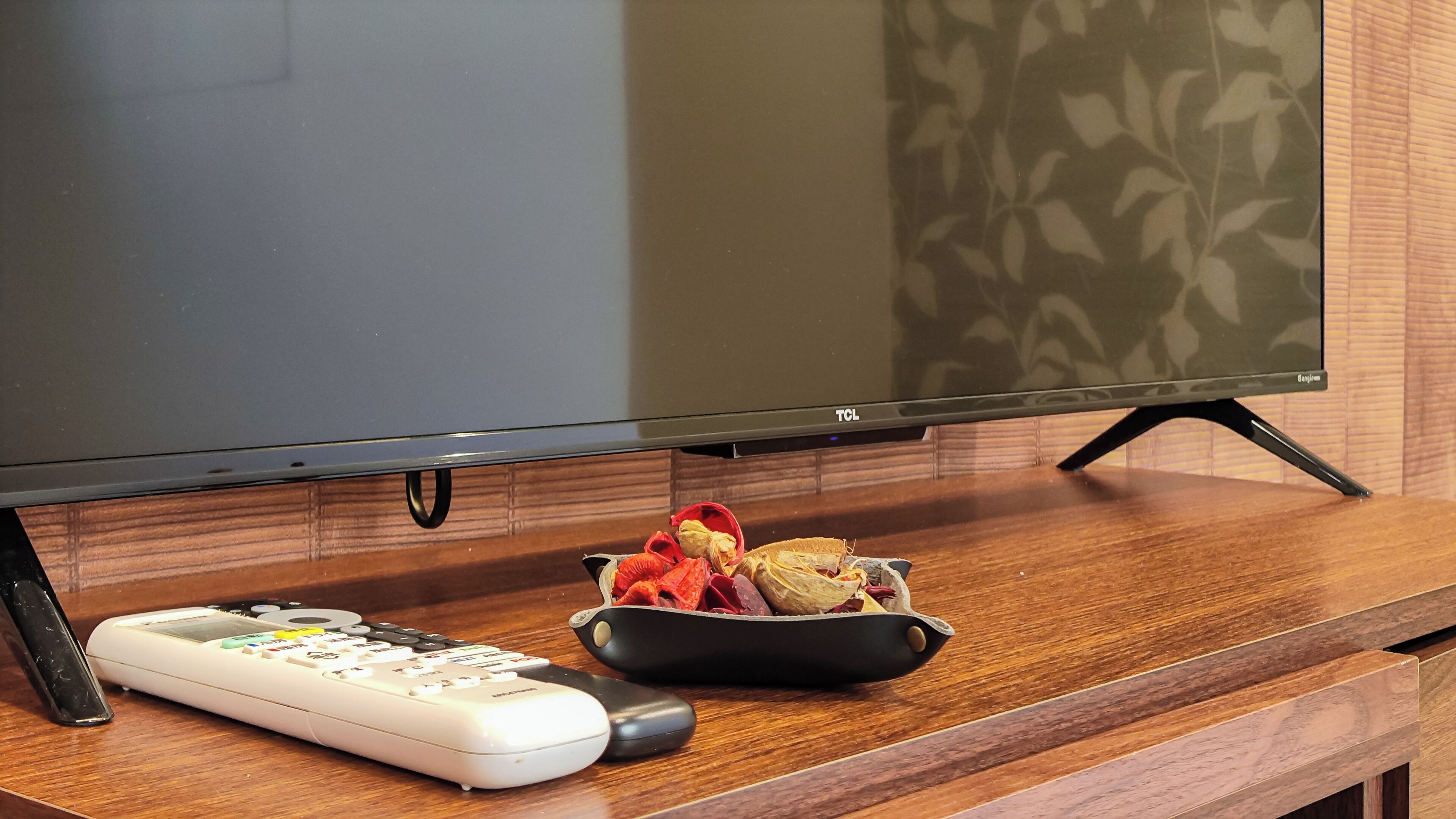 Un mueble bajo de madera con un televisor de pantalla plana, un control remoto y un tazón de aperitivos.