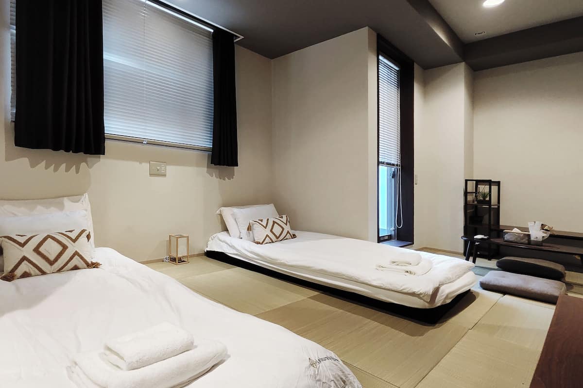 Hotellihuone, jossa on kaksi erillistä sänkyä, pieni työpöytä, tuoli ja ikkuna, jossa on sälekaihtimet.