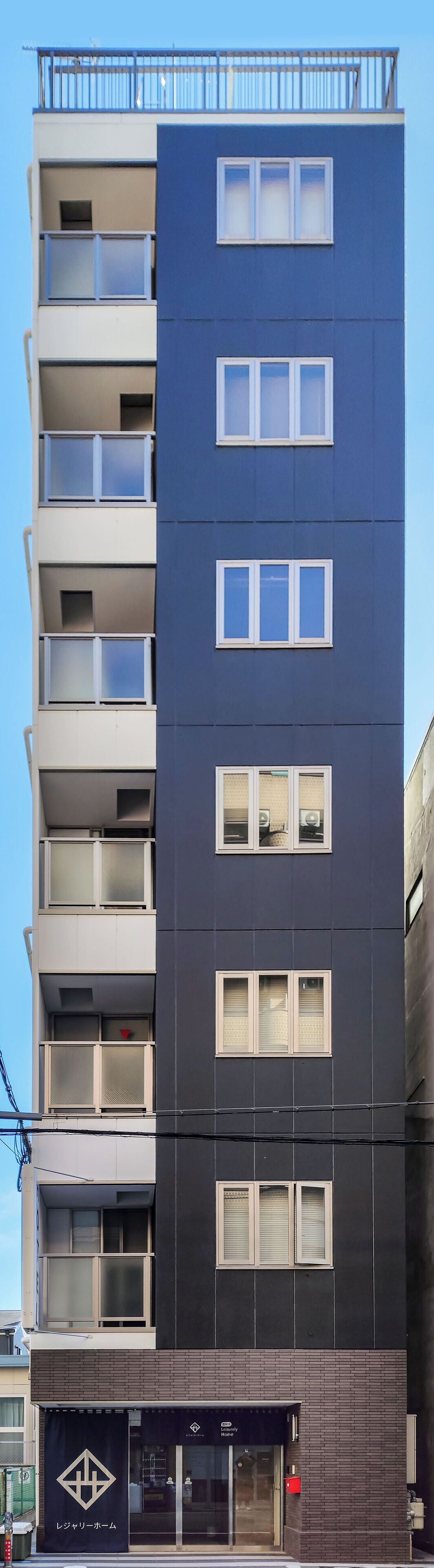 Un immeuble à plusieurs étages, doté d’une façade sombre, de nombreux balcons et d’une vitrine au niveau du rez-de-chaussée.