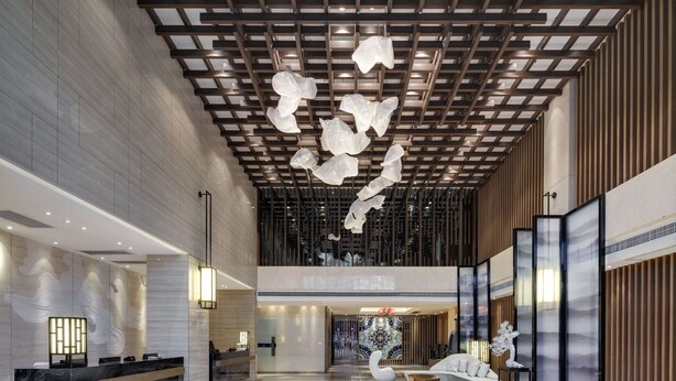 Un moderno vestíbulo de hotel con mostrador de recepción, zona de estar y detalles decorativos en el techo.