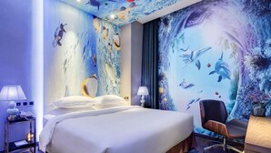 Habitación de hotel con una cama, un escritorio, una silla y un mural en la pared que representa escenas submarinas.