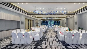 Un salón de banquetes con mesas redondas, sillas blancas y una alfombra estampada.