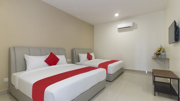 Habitación de hotel con dos camas, cada una con ropa blanca y detalles rojos, una mesita y un equipo de aire acondicionado en la pared.
