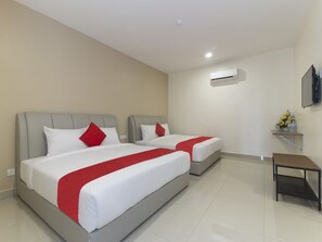 Una habitació d'hotel amb dos llits, cada un amb roba de llit blanca i detalls vermells, una taula petita i una unitat de aire condicionat a la paret.
