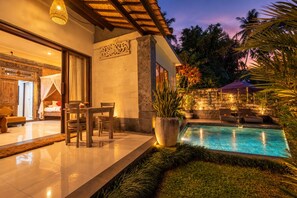 A well-lit outdoor pool area with a dining table and chairs, surrounded by lush greenery and a stone wall. - Taluh Bebek Ubud Private Villas (Ubud)