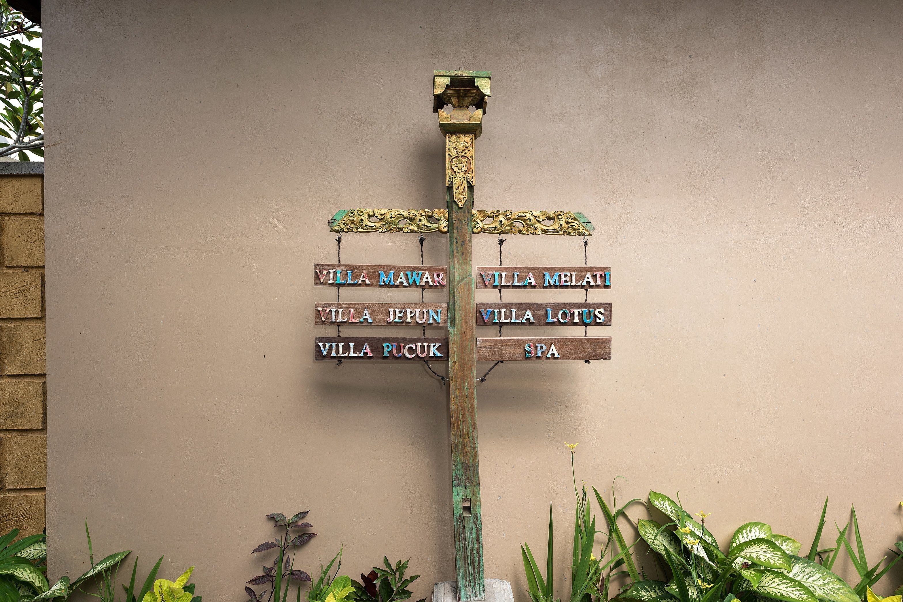 A wooden signpost with multiple directional signs pointing to different villas and a spa.