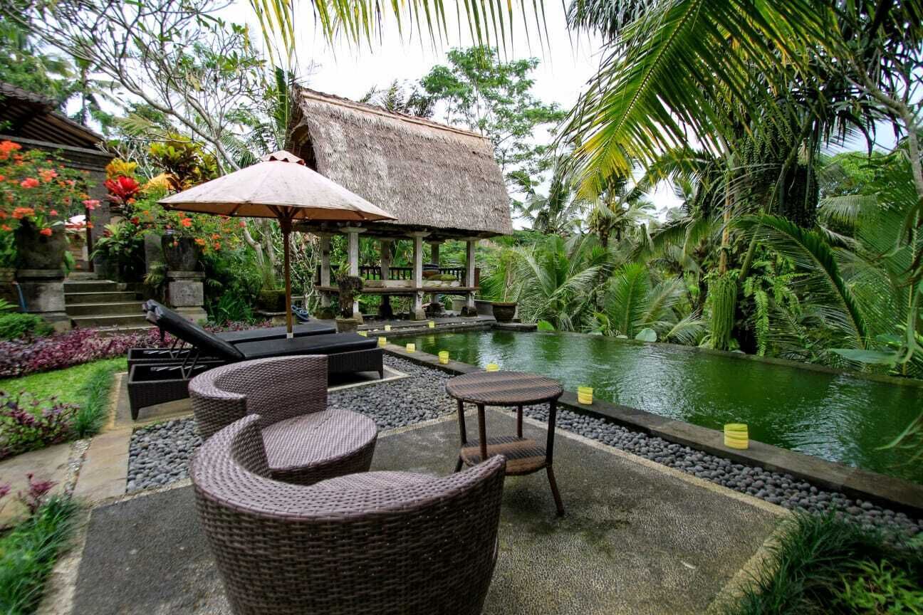 A tropical outdoor seating area with wicker furniture, a thatched-roof structure, and a small pool.