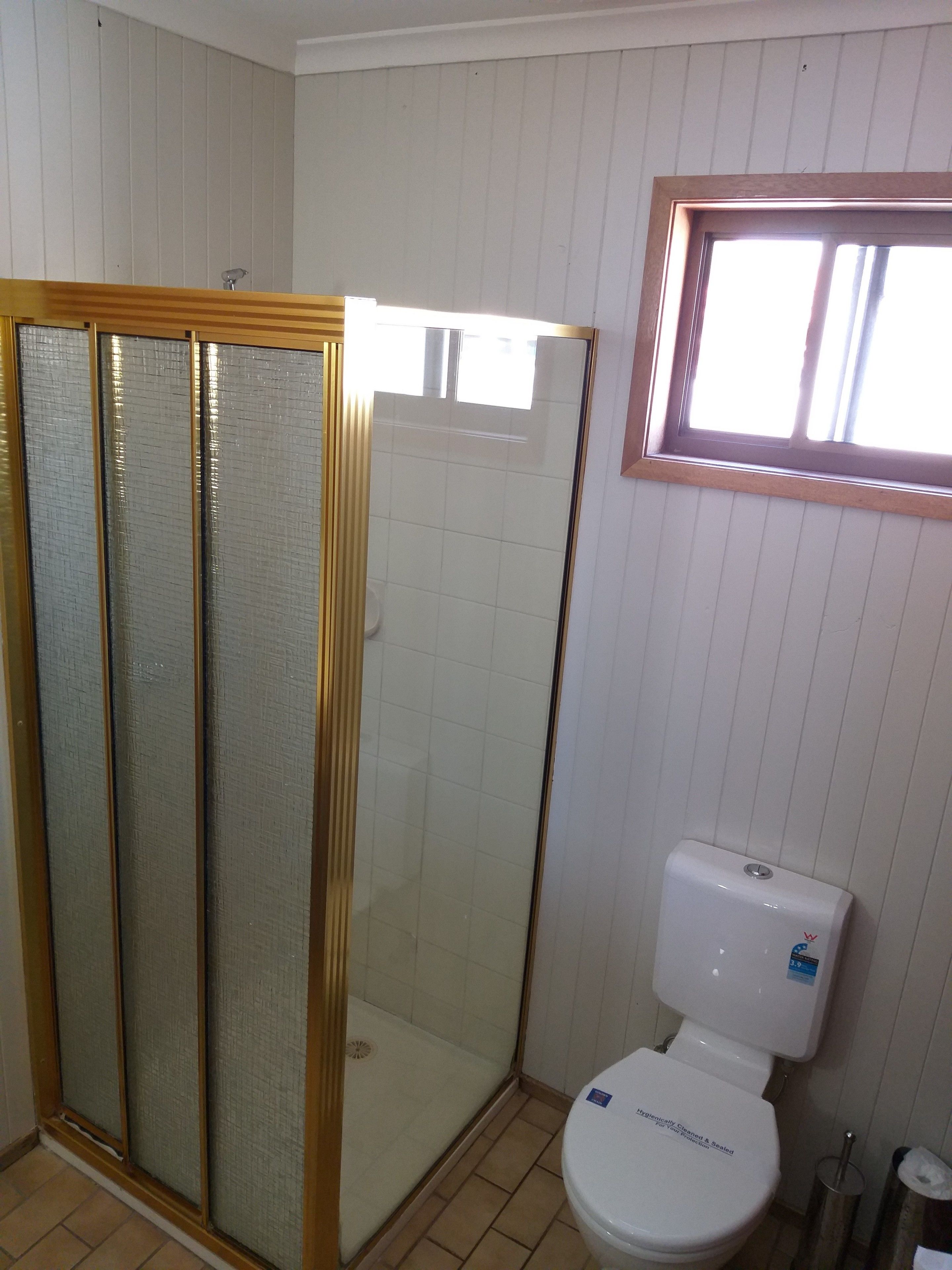 Ett badrum med en dusch som är avskärmad med glasväggar, en toalett och ett fönster ovanför toaletten.