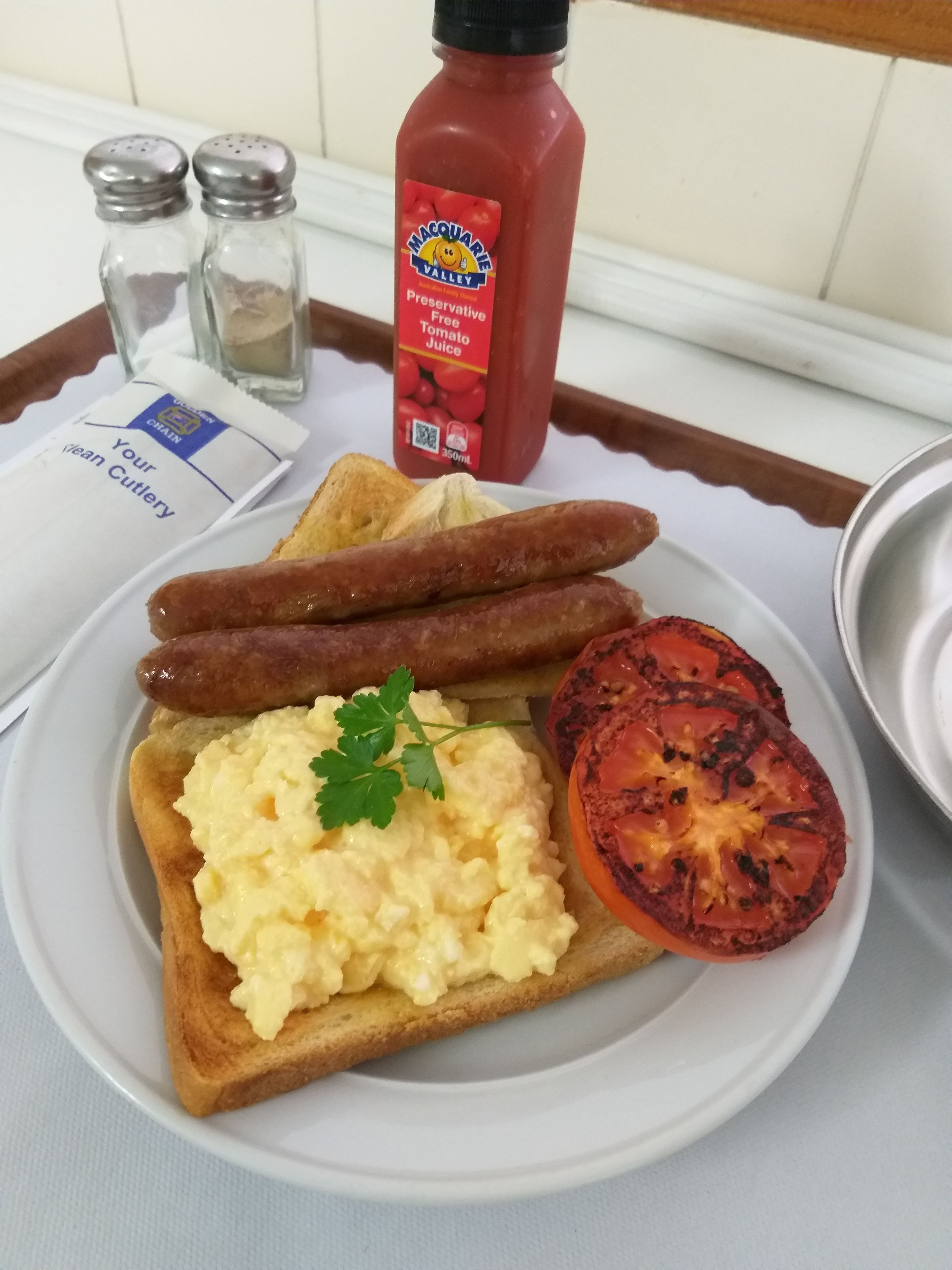 Een ontbijtbord met toast, roerei, worstjes en een gegrilde tomaat.