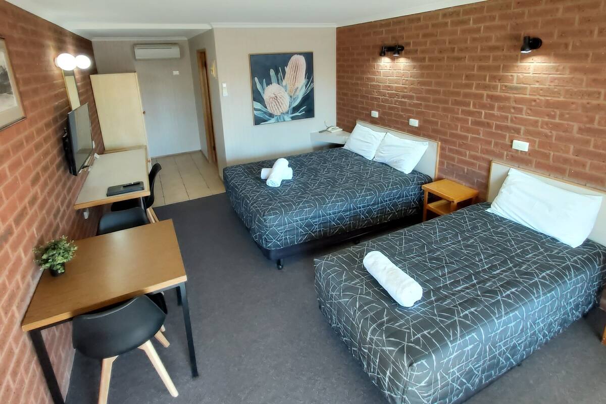 A hotel room with two beds, a desk, a chair, and a small table.