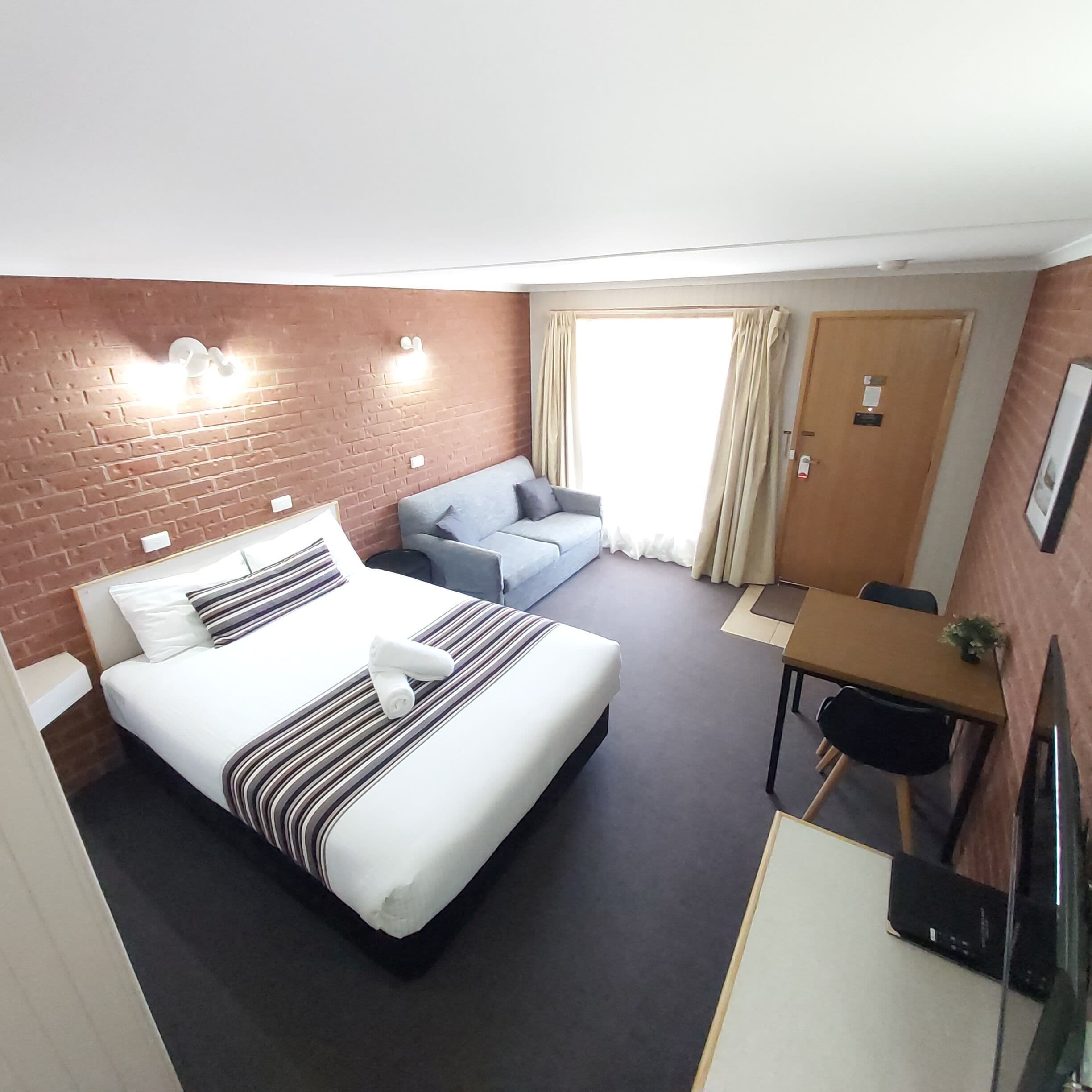 Ein Hotelzimmer mit einem Bett, einer Couch, einem Schreibtisch und einem Fenster mit Vorhängen.