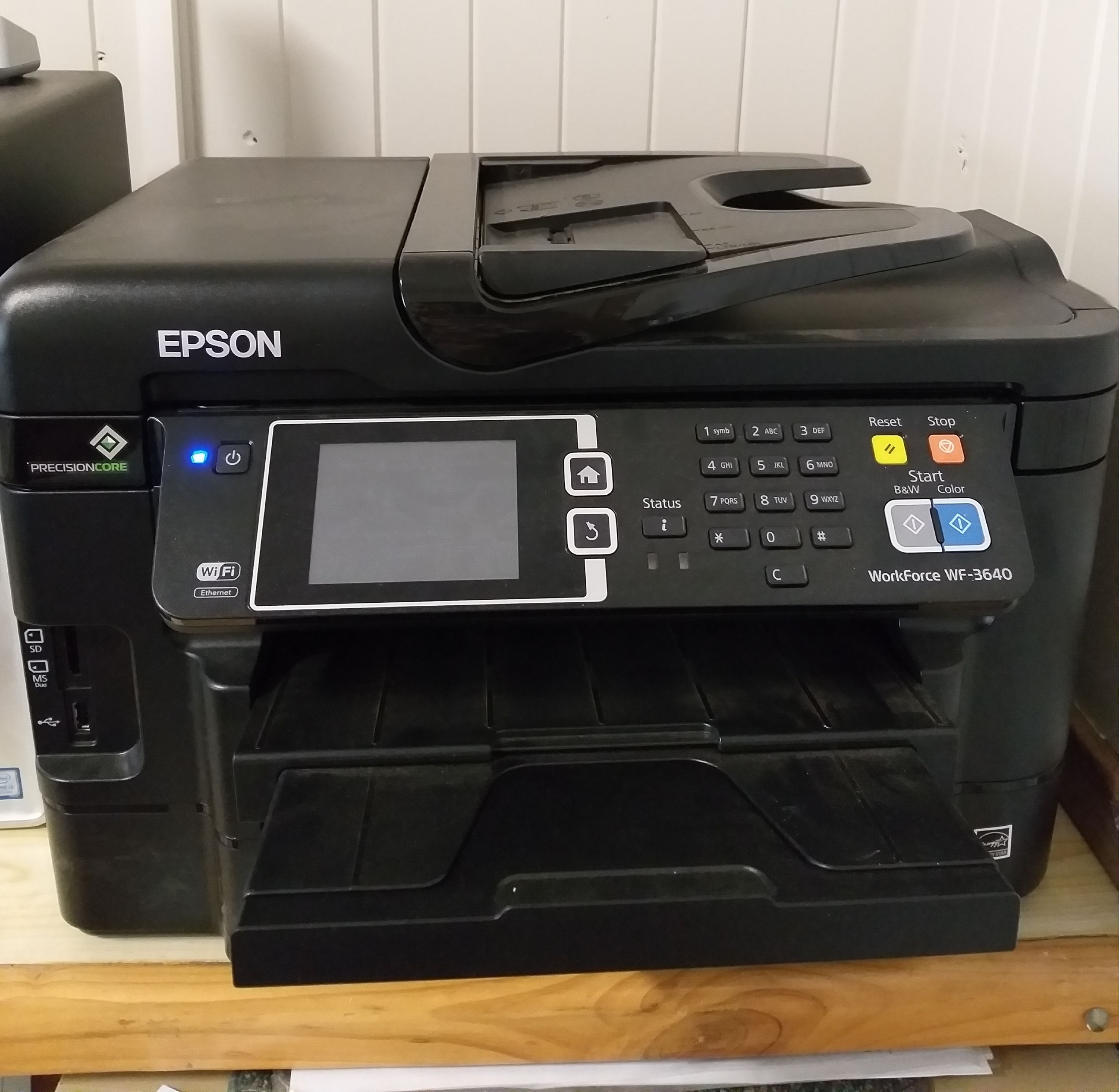 A black Epson printer with a touchscreen interface, Wi-Fi and Ethernet connectivity, and a paper output tray.