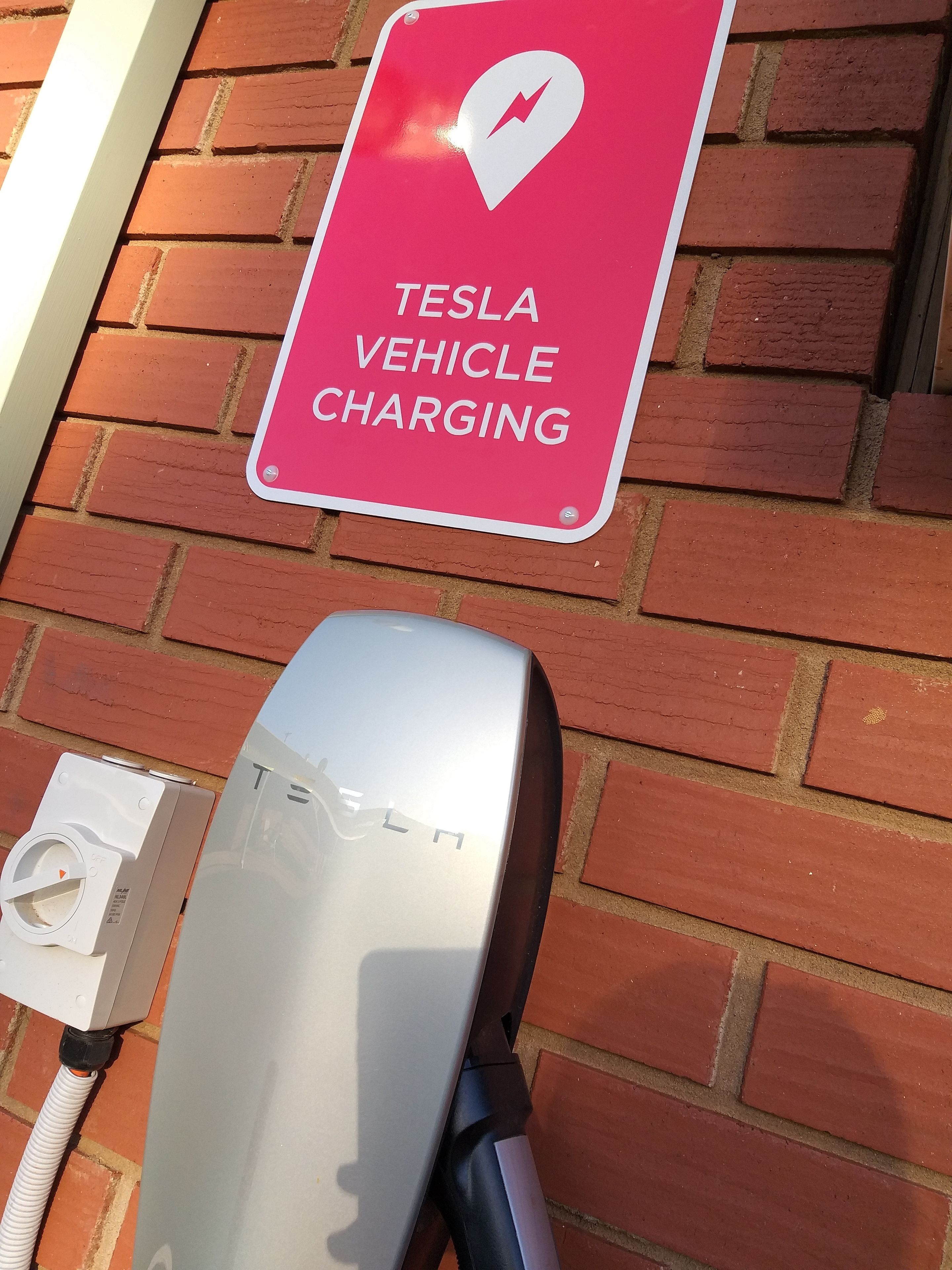 Una estación de carga para vehículos Tesla con un letrero rojo que indica 'TESLA VEHICLE CHARGING'.