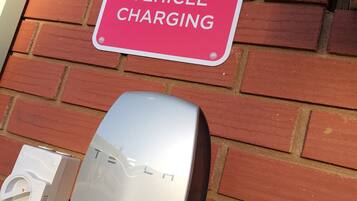 Una estación de carga para vehículos Tesla con un letrero rojo que indica 'TESLA VEHICLE CHARGING'.
