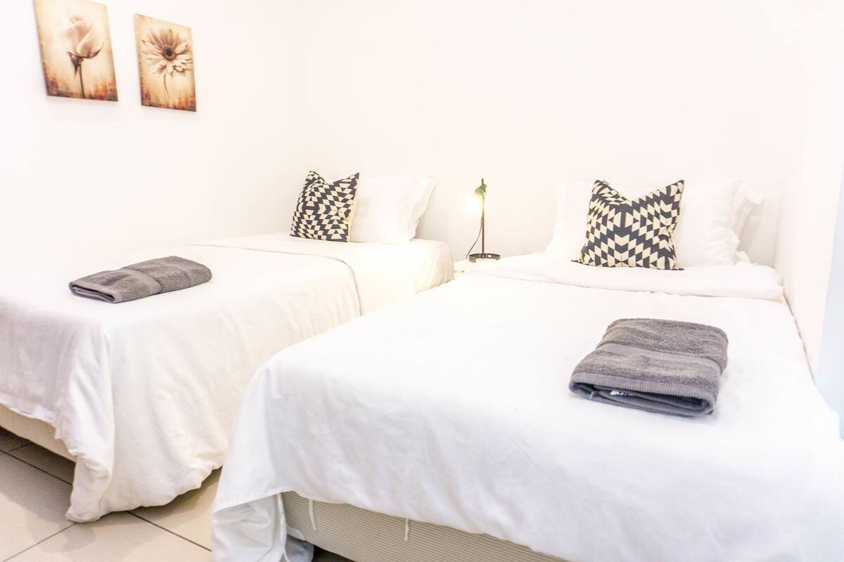 A hotel room with two single beds, each with a pillow and a folded towel.