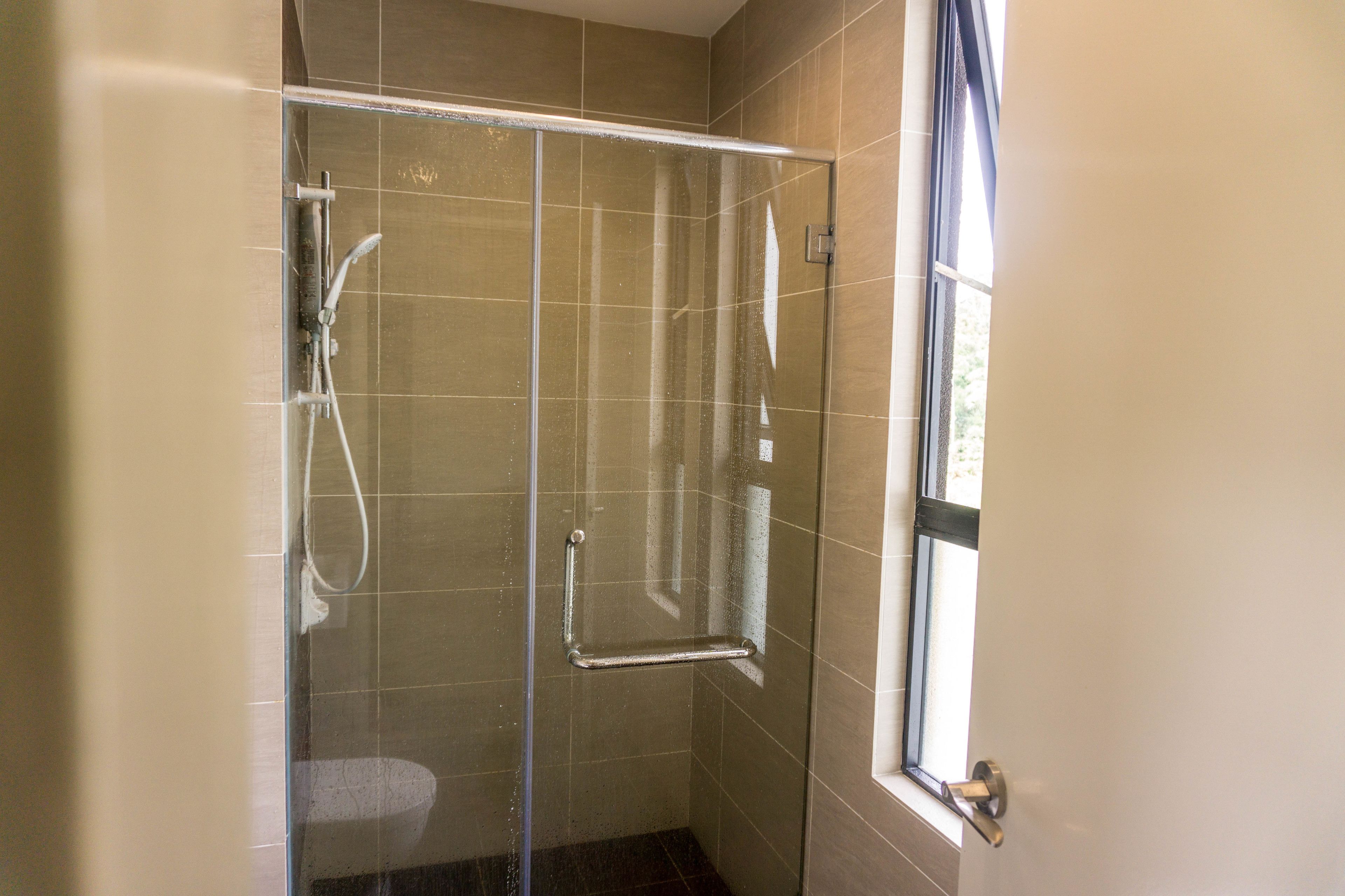 A glass-enclosed shower with a handrail, a window, and a door.