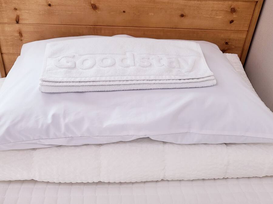 A neatly made bed with a folded white towel on top and a pillow.