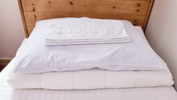 A neatly made bed with a folded white towel on top and a pillow.
